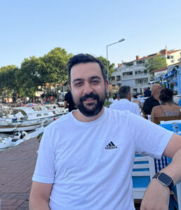 Picture of Ferhat standing outdoors, wearing a white t-shirt.